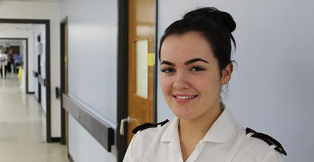 Apprentice standing in a corridor at Arrowe Park Hospital wearing a white uniform