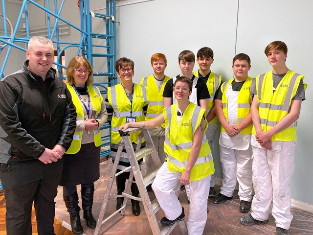 painting and decorating students and apprentice in white overalls and high vis vests stood in school next to teachers and employer