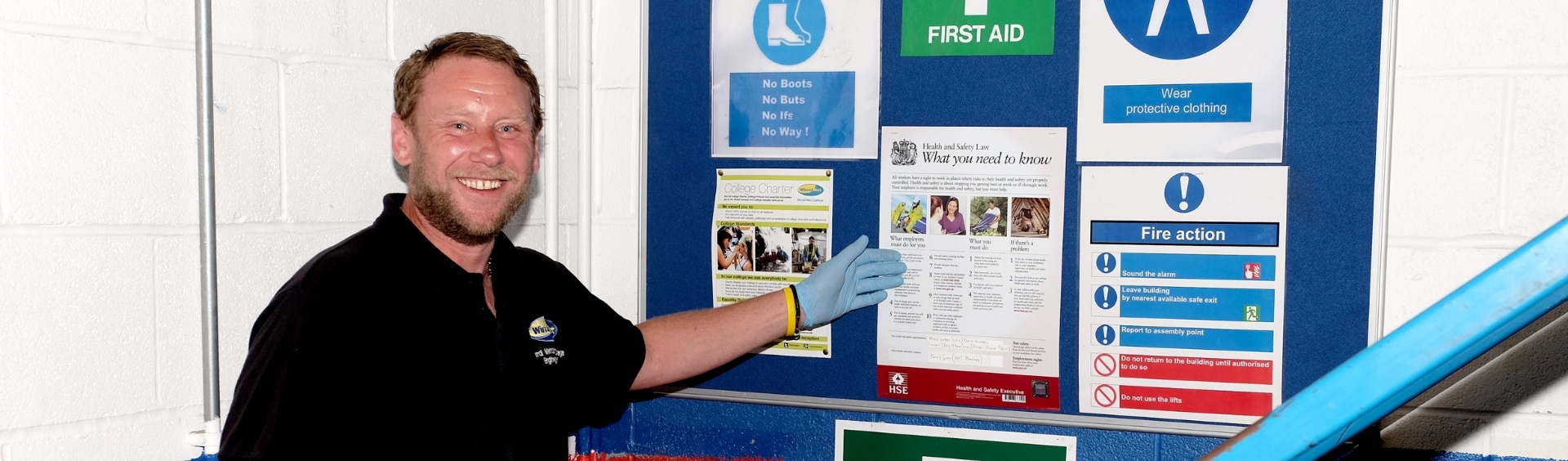 WMC Risk Assessment student pointing at Health & Safety noticeboard in classroom