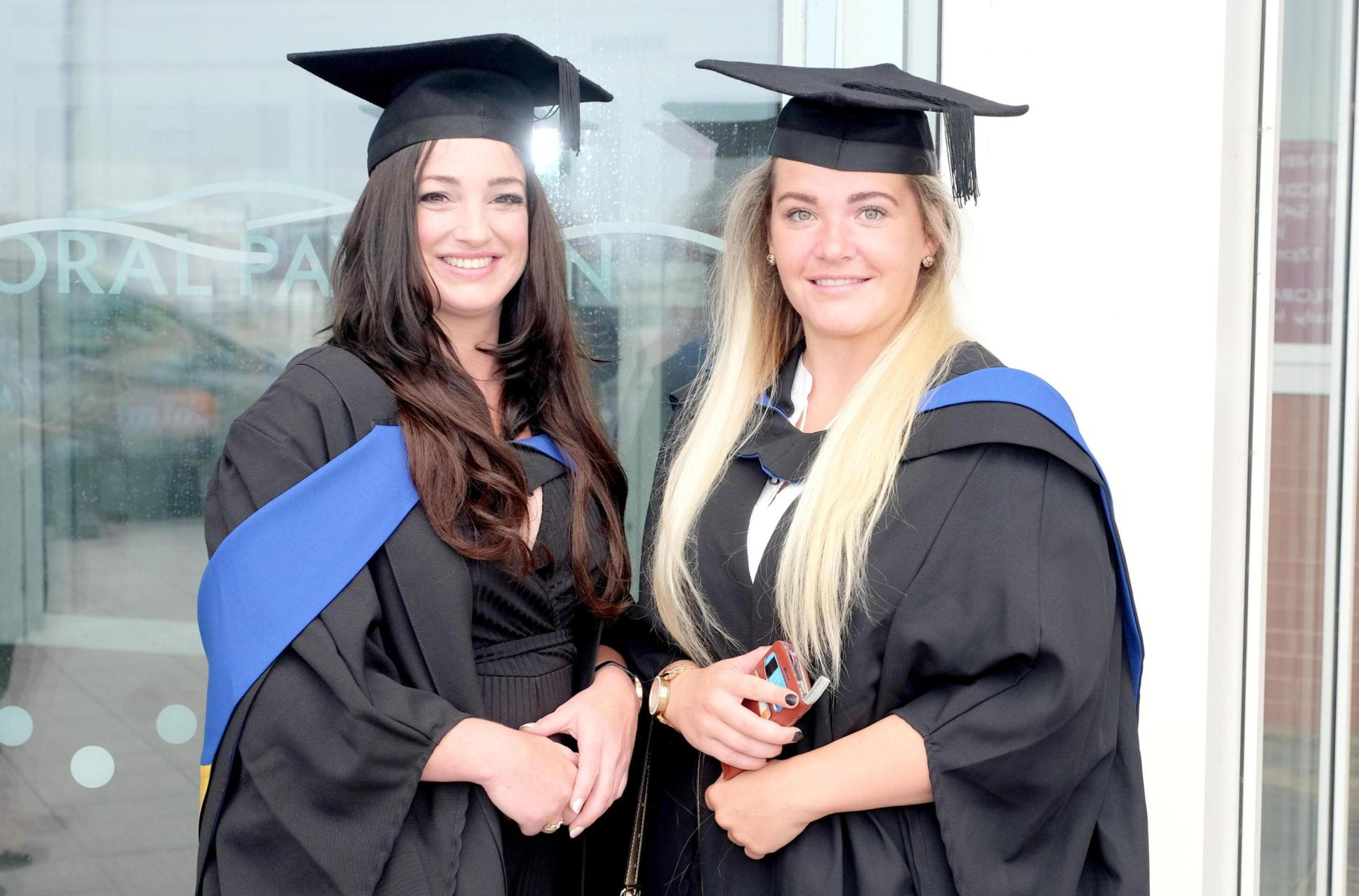 Two Female Wirral Met Higher Education Students wearing Graduation Gowns and Caps