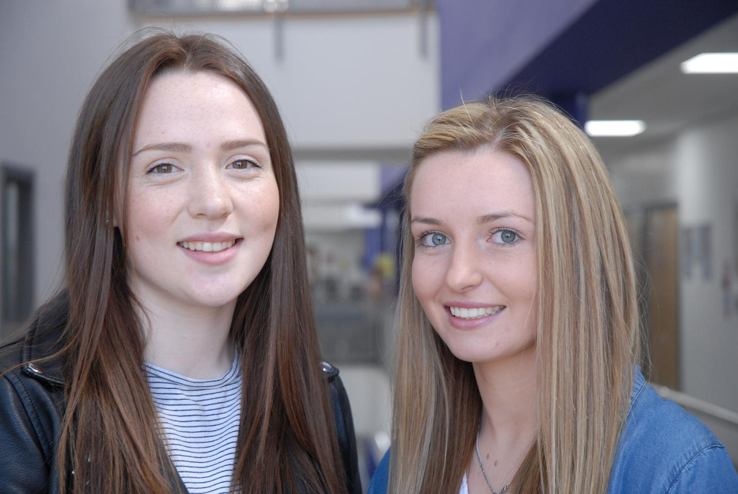 Two female Wirral Met students smiling and standing in a corridor