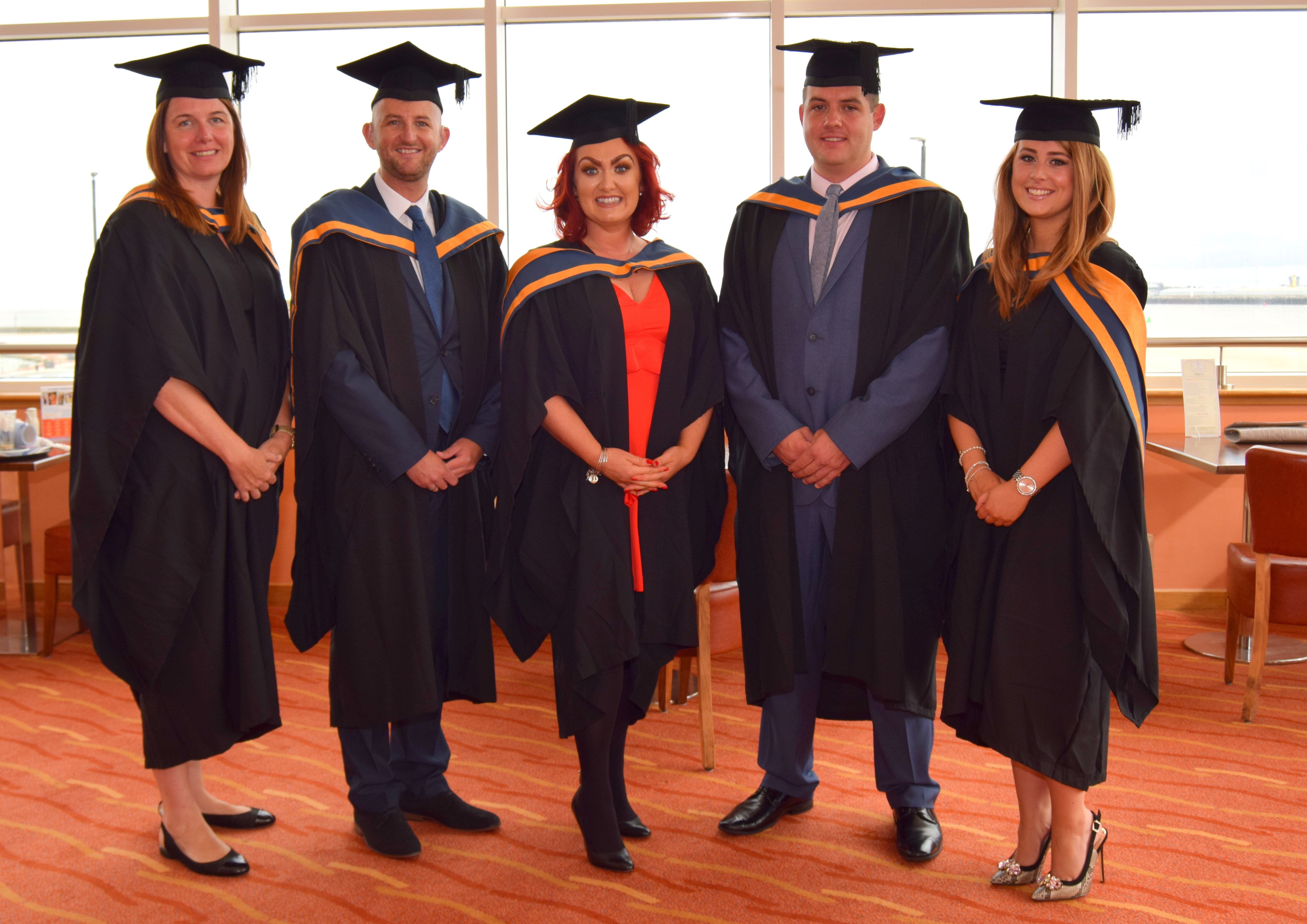 Wirral Met Higher Education graduates wearing gowns and standing on an orange carpet