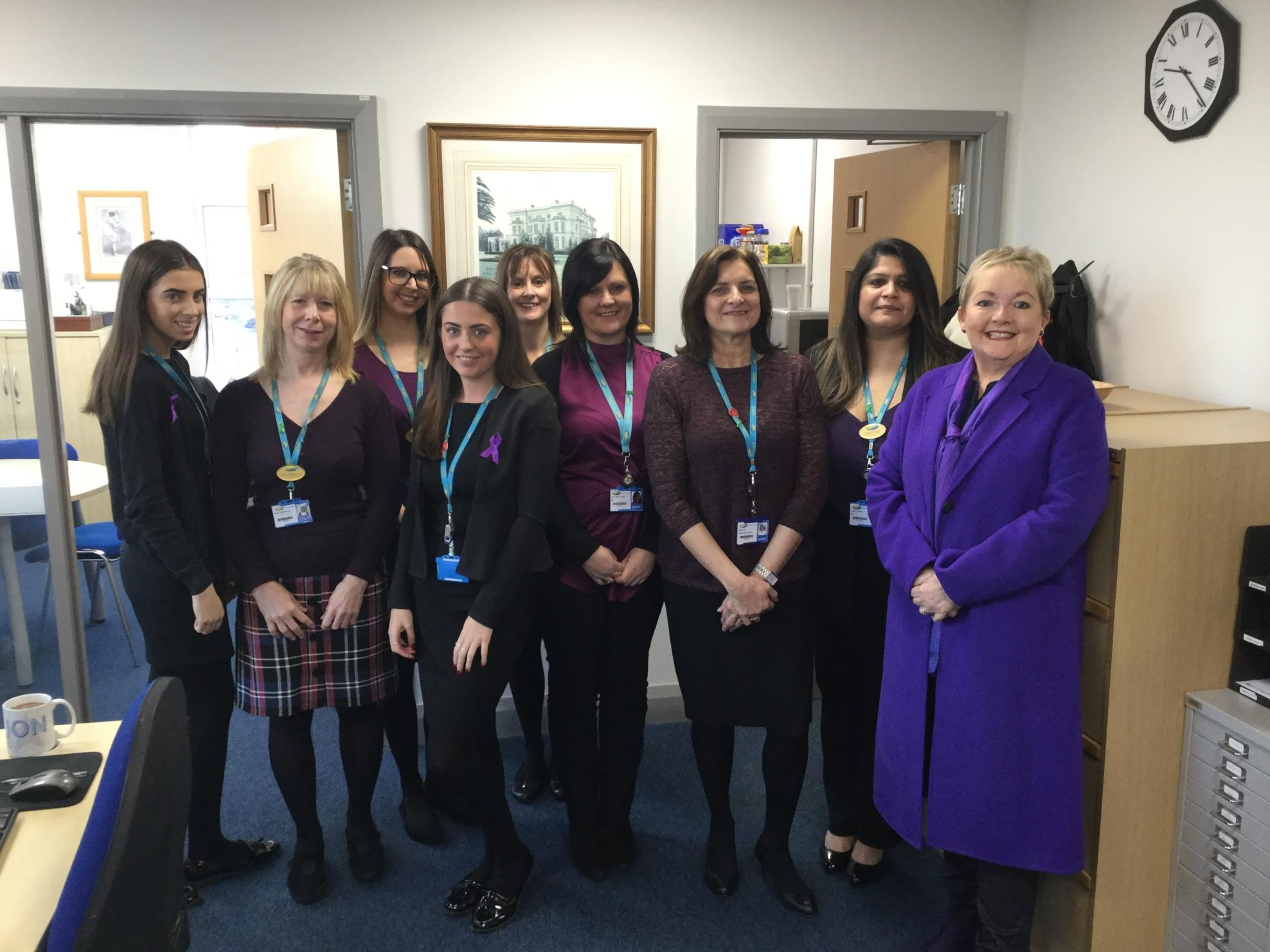 Nine Wirral Met College staff members stood in an office wearing purple clothing to support International Day for Persons with Disabilities