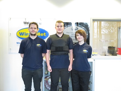 Three Wirral Met Public Services Students wearing Safeguard Armour with Wirral Met logo on a wall behind them