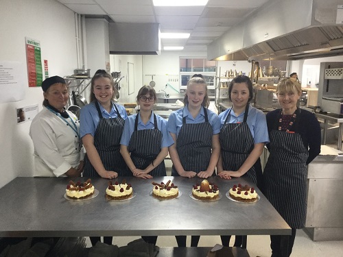 West Kirby Grammar School students standing in front of a table of cakes wearing aprons alongside teachers during Pastry Masterclass at Wirral Met College