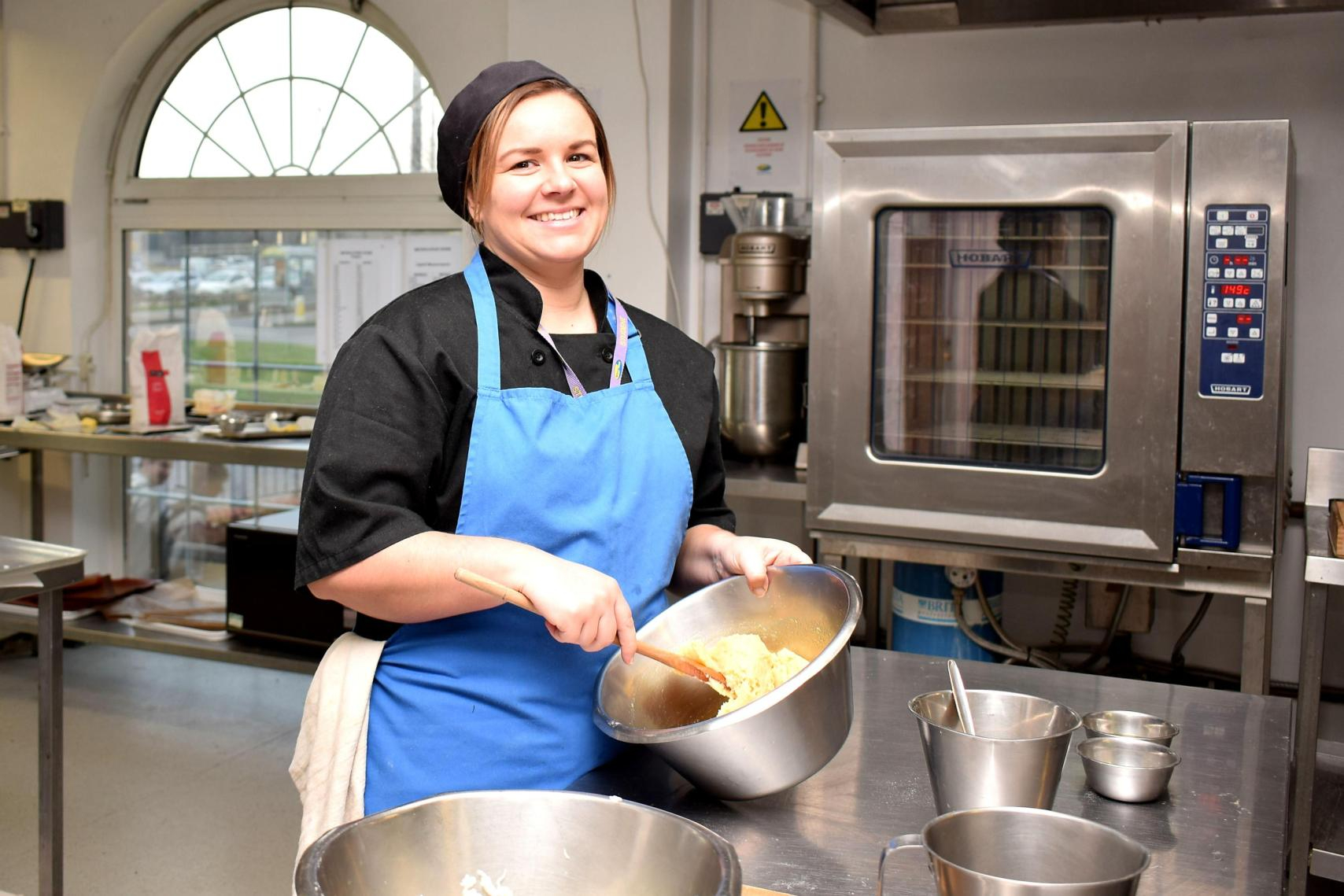 Female catering student in training kitchen mixing ingredients in a bowl