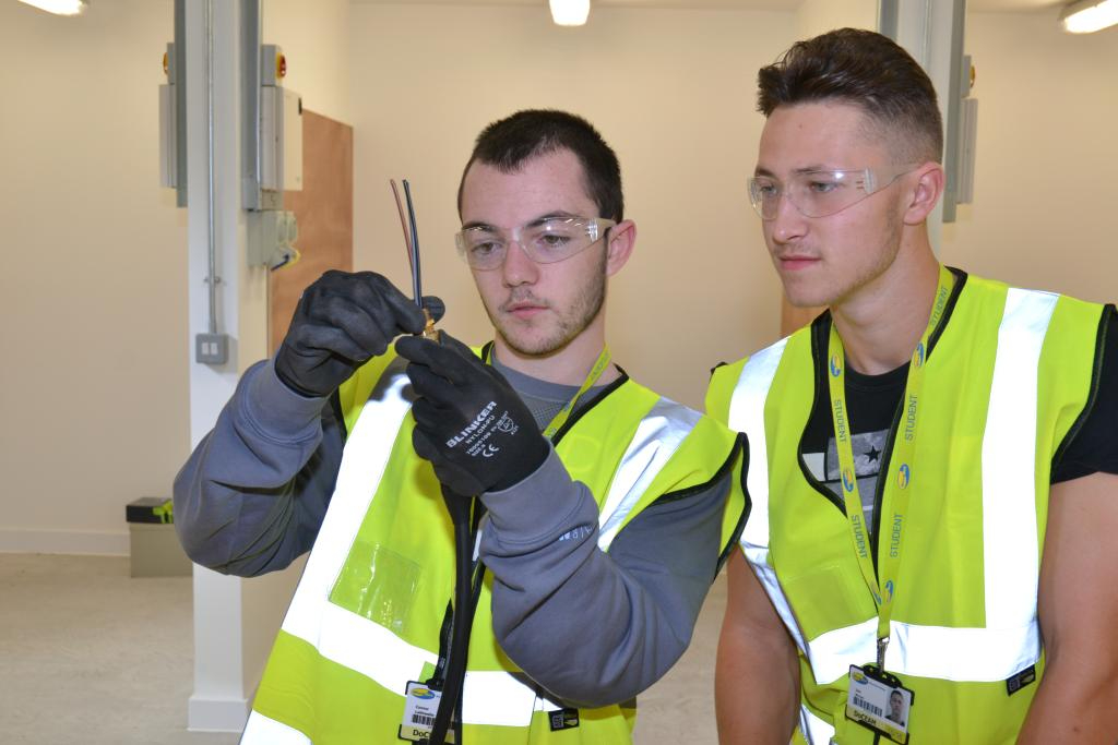 Two Wirral Met students wearing Hi-Vis Jackets examining a piece of wire
