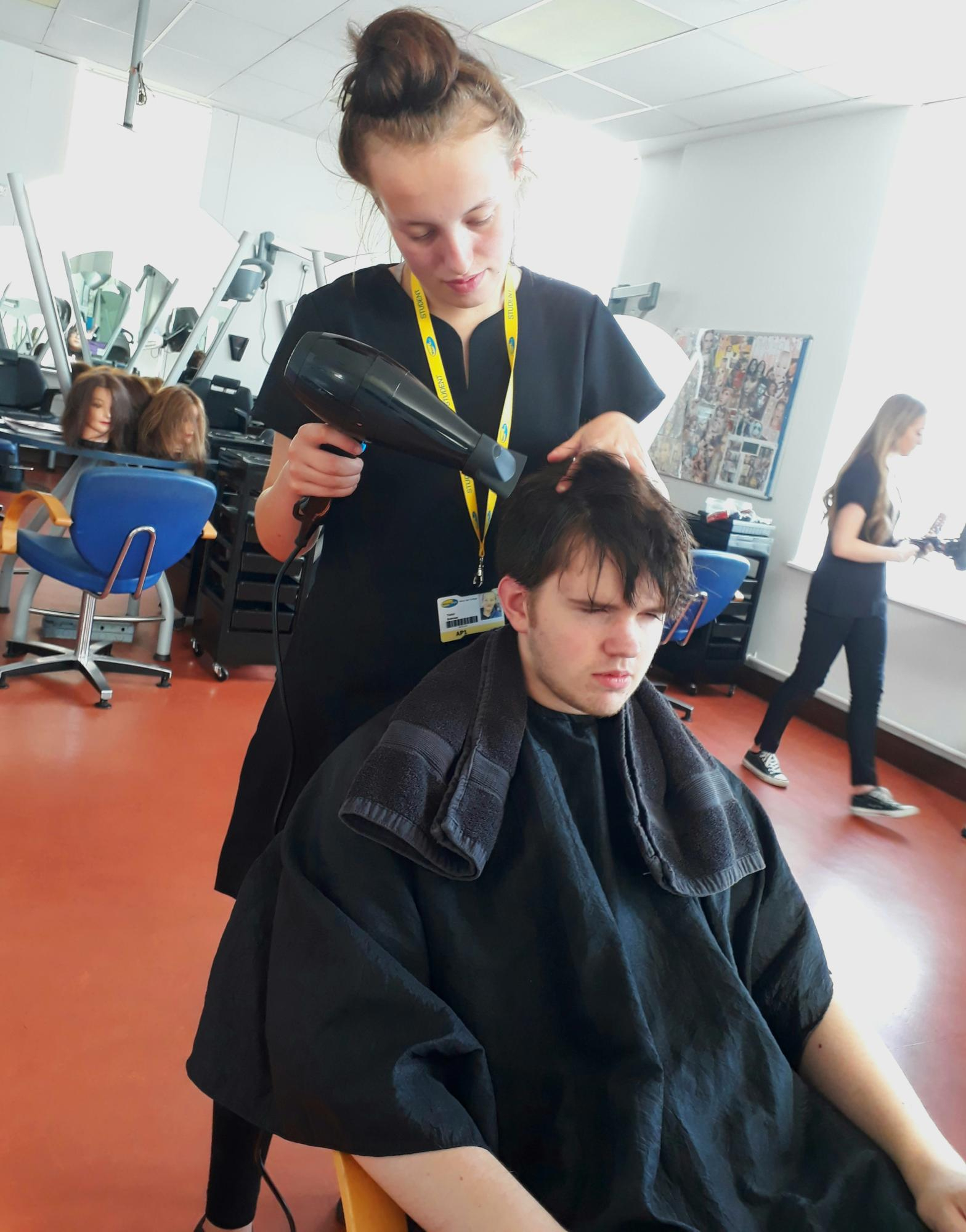 Wirral Met Hair and Beauty student wearing yellow lanyard blow drying a boy's hair 