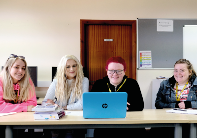 Four Part Time Social Studies Students Sat At Long Table In Classroom