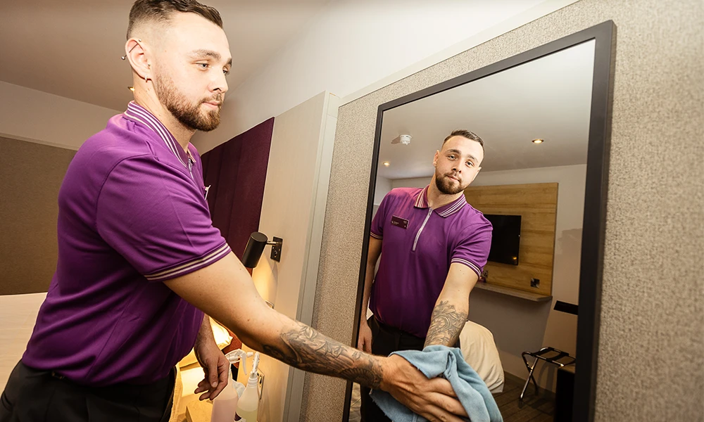 A male in purple uniform washing a mirror with a blue cloth