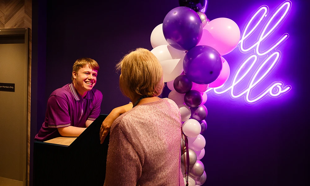 a male with purple uniform smiling on a desk with purple balloons