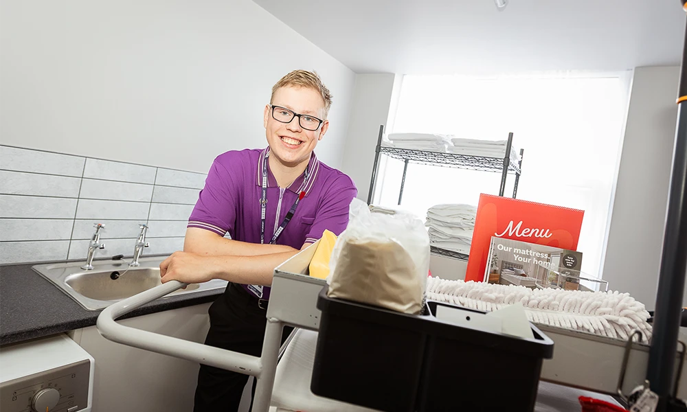 Male leaning on a cleaning cart in a purple uniform