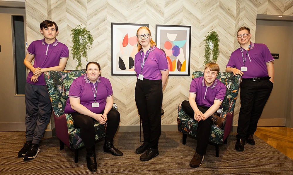 3 students standing and 2 sat down all in purple uniform