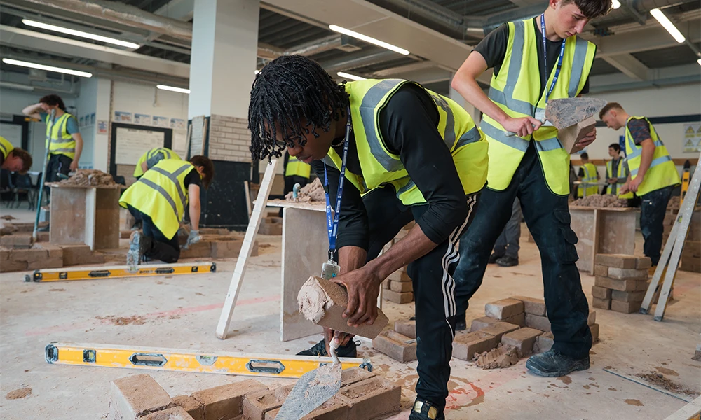 Bricklaying student holding trowel whilst standing inside workshop