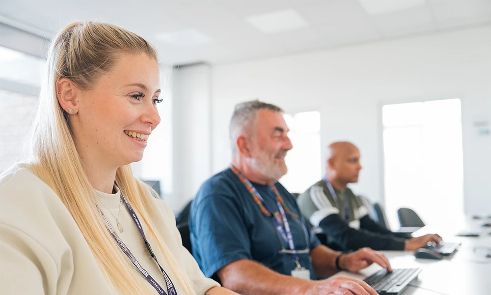 Three adults sat at a desk with a computer in front of them