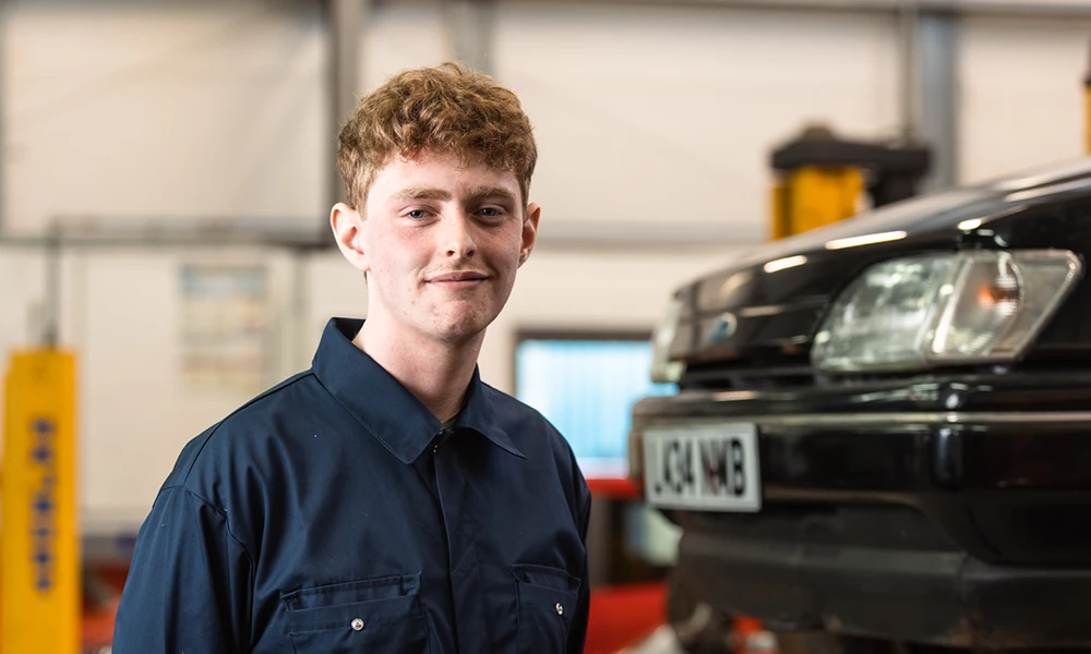 A student stood next to a car in a workshop