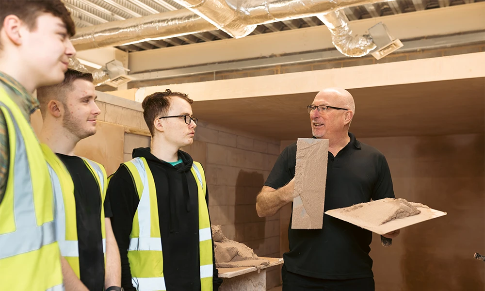 Three male students with a tutor plastering