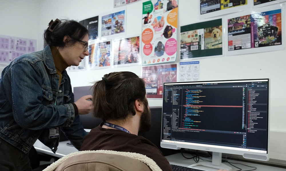 Games Design student coding on college computer with help from course tutor