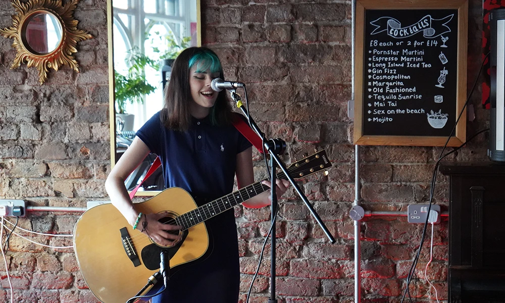 Female student Singing into a microphone with a guitar