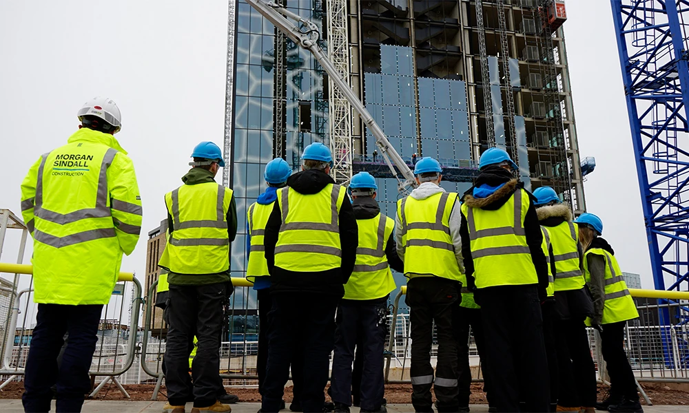 A group of people wearing hi-vis jackets in front of building site