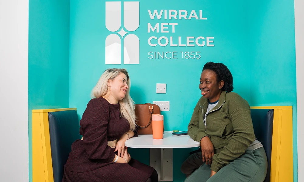 Two women at across from each other with the wirral met logo in the background