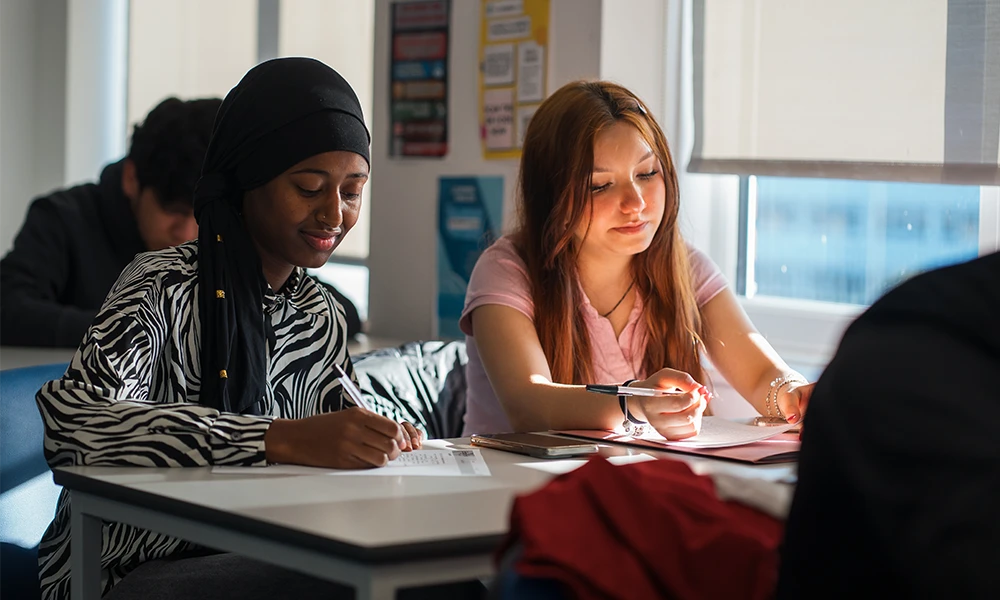 Two girls sat at a desk writting