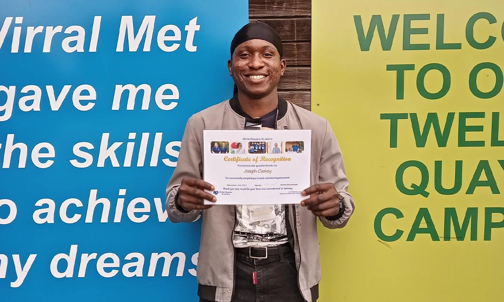 Man Stood Infront of building holding a sign saying congratulations from Wirral Hospice