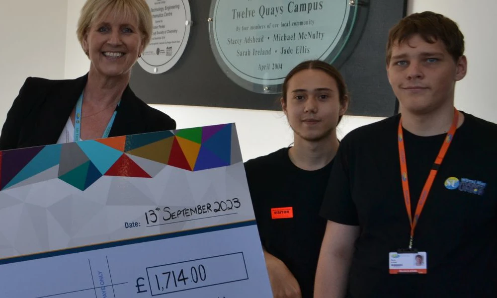 Principal Gill Banks holding a giant cheque whilst standing next to students