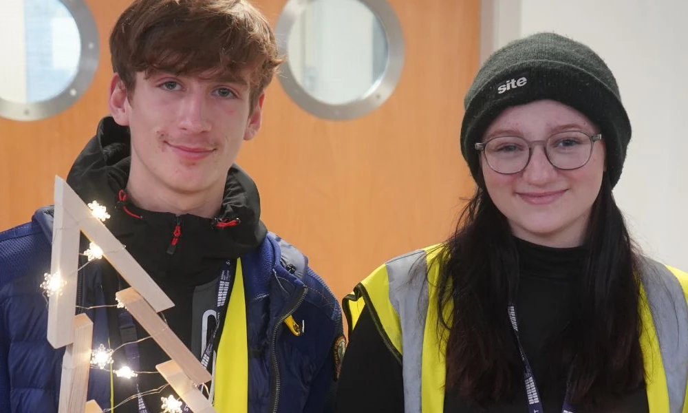 Two Wirral Met construction students holding handmade wooden Christmas Tree at Hamilton campus event