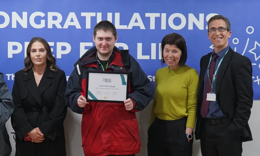 Wirral Met staff and students posing in front of congratulatory banner for Beacon Awards
