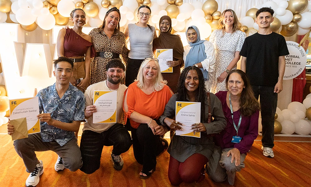 Group of English For Speakers of Other Languages students posing with their tutor in front of bright Wirral Met sign