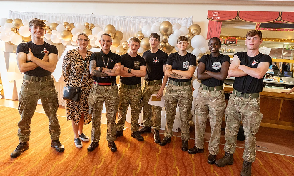 Group of Military Preparation students folding their arms as they stand next to their tutors in front of bright Wirral Met sign