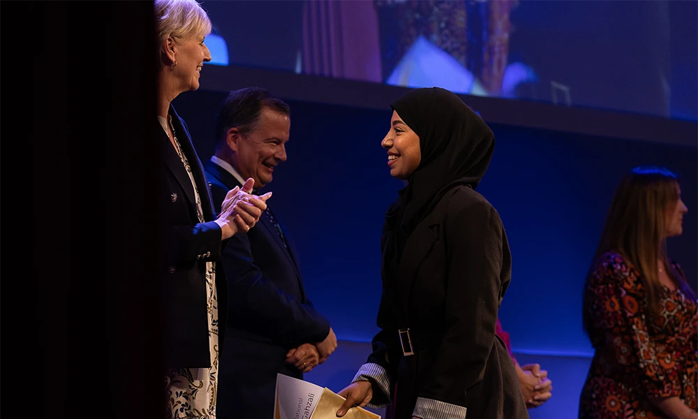 Female student greeting members of the Senior Leadership Team on stage