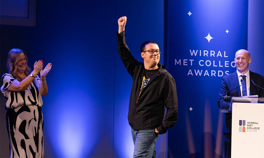 Male student raising his hand into the air as he walks across the stage