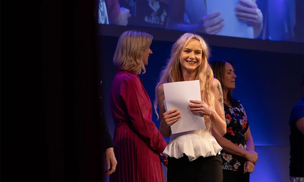 Female student smiling as she holds her certificate on stage