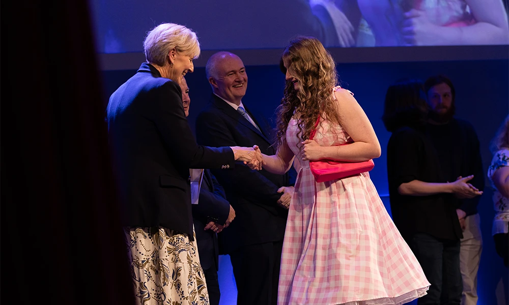 Female student shaking hands with the Principal as she collects her certificate on stage