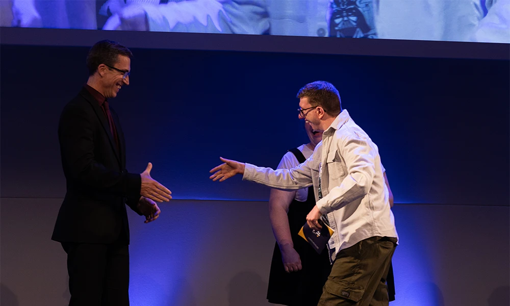 Male student shaking hands with member of the Senior Leadership Team as he crosses the stage