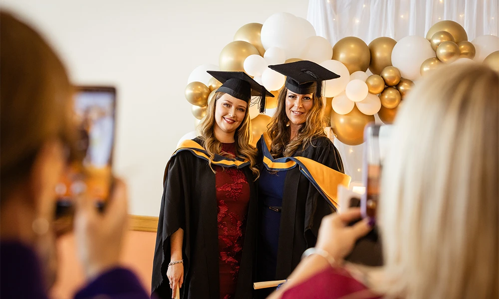 Two women in graduation cap and gowns getting a photo