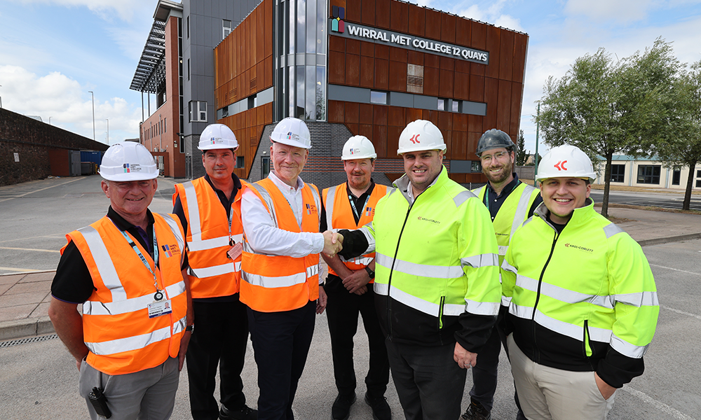 Seven men infront of a building smilling with hi vis jackets on