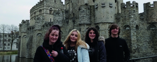 four students standing in front of a castle wearing coats