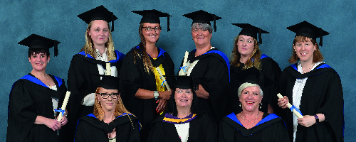 Higher Education graduates wearing gowns posing for group picture with a blue background