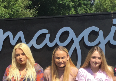 three students sitting outside in front of a shop sign wearing pink and purple t-shirts